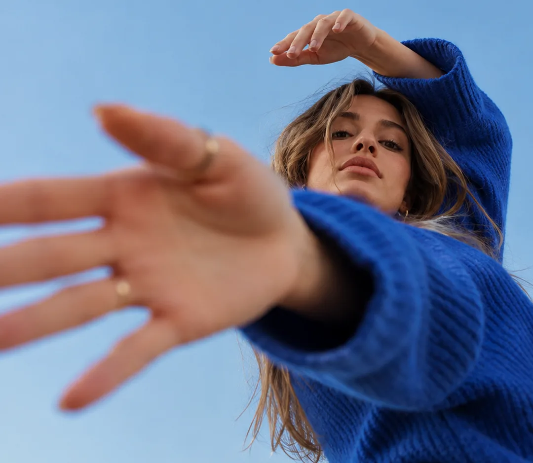 Una chica con jersey azul extiende la mano hacia la cámara