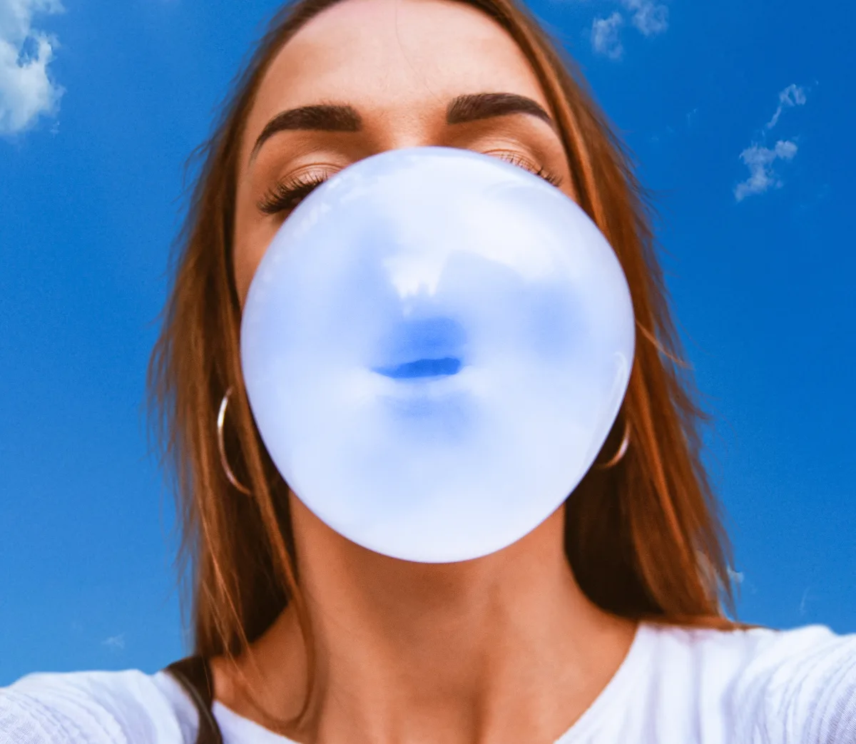 Una chica hace un globo de chicle con el cielo azul de fondo